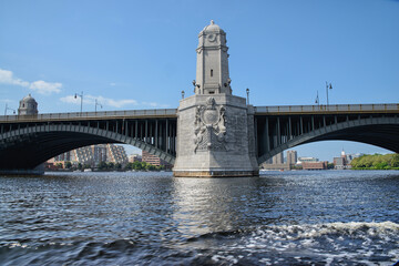 The majestic Longfellow Bridge in Boston with its ornate stone towers and elegant arches, reflecting on the calm waters of the Charles River under a clear blue sky.