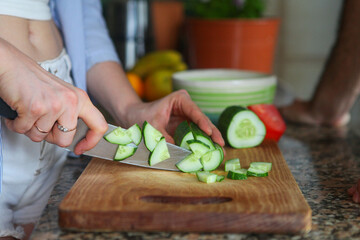 closeup of hands of woman cutting fresh vegetables for salad at home