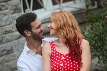 portrait of young smiling couple in love outdoors on summer day with house wall in background