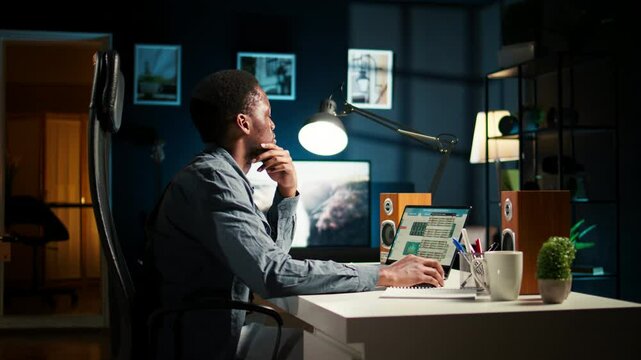 Black young adult working remotely and organizing information, reviewing notes and making data driven decisions to complete his freelancing tasks. Managing his schedule efficiently. Camera A.
