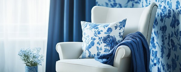 White armchair with blue floral pillow and draped blanket, placed next to blue floral cyanotype effect patterned wall and blue curtains, creating serene and elegant reading nook with natural light