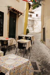 A charming outdoor café with floral tablecloths set along a narrow cobblestone alley in a European town, evoking a rustic ambiance. Vertical stock photo