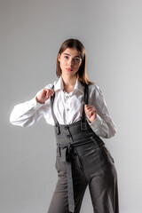 Young model poses confidently in stylish gray outfit with white shirt against a minimalist gray...