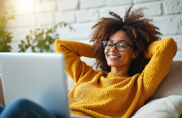 Smiling African-American woman relaxing on couch with laptop at home. Successful freelancer rests, enjoys peace of mind using pc, browsing web. Online shopping, work, remote connection, networking,