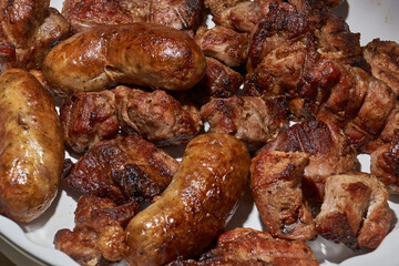 Skewered kebabs and homemade sausages in a white porcelain mold. Close-up.