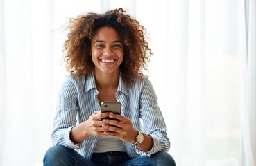 Smiling African American girl holds phone, dials number. Woman texts message, reads email, browses social media, makes video call. Beautiful curly hair model in jeans using smartphone app.