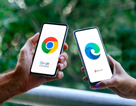Hands of two people with mobile phones showing the chrome browser on one and microsoft edge on the other. Rosario, Argentina - March 8, 2025.