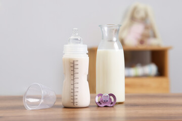 Milk in feeding bottle, jug and pacifier on wooden table indoors