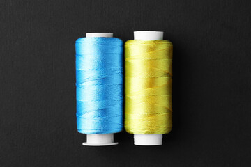 Spools of colorful sewing threads on black background, top view