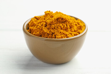 Turmeric powder in bowl on white wooden table, closeup