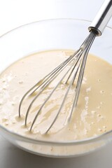 Whisk and bowl of dough on table, closeup