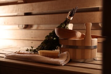 Massaging brush, towel, bucket, whisk and ladle on wooden bench in sauna