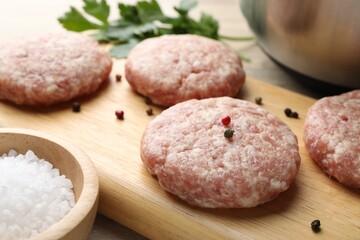 Many uncooked patties and spices on wooden table, closeup