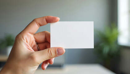 Fototapeta premium Close-up of hand holding blank business card. Workplace office environment background for corporate identity design template. Mockup concept for pro branding, advertising, marketing, presentation,
