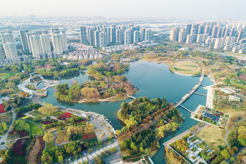 Aerial view of a lush urban park featuring water bodies and pathways amidst modern cityscape