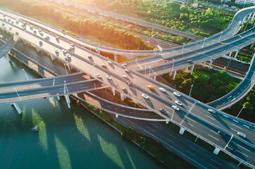 Aerial view of multiple highways intersect above a calm river, surrounded by vibrant greenery.