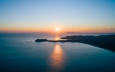 Golden sunset casts shimmering reflections over calm ocean waters in tranquil coastal landscape