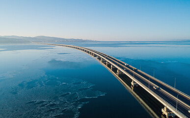 Aerial view of a long road bridge stretching over calm waters at dawn with distant mountains and...