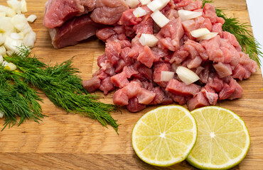 Fresh raw meat with dill, lime and vegetables on wooden background, close-up