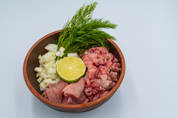 Raw finely chopped beef, onion, celery root, dill and lime in a plate on a white background. Ingredients for Serbian soup chorba.