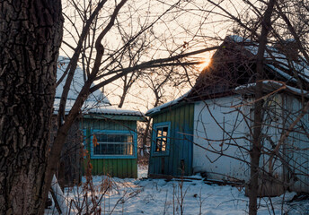 Winter sunset illuminating abandoned buildings in a rural setting with snow-covered ground.