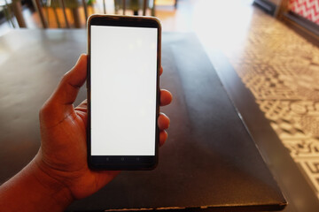 Hand holding a smartphone in a cafe setting during daylight hours