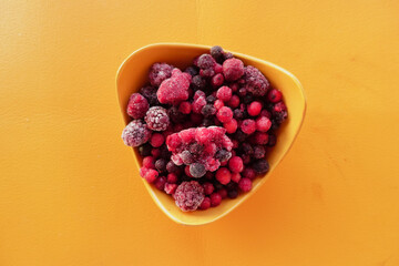 Frozen mixed berries in a yellow bowl on an orange surface