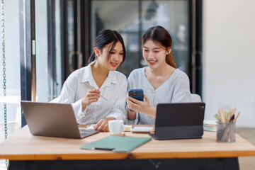 Fototapeta premium Two happy business asian women coworking with a laptop in a desktop at office 