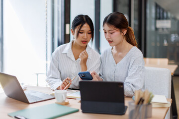 Two happy business asian women coworking with a laptop in a desktop at office
