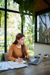 Businesswoman working on a laptop with documents in a natural-themed office, focused and determined on business tasks.