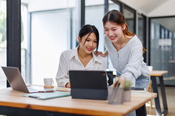 Two smiling happy asian businesswomen working together on a laptop in the office, demonstrating teamwork business meeting in a corporate and collaboration
