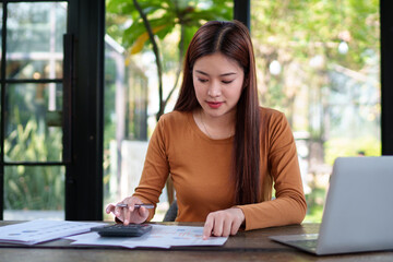 Businesswoman analyzing financial documents at a natural-themed office, focusing on charts and data...