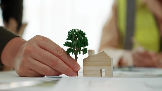 A video of architect using tree and home model to measure blueprint. Architect designing house construction on a table at studio, with architectural plan scattered around. Focus on hand. Delineation.