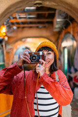 Obraz premium Young beautiful smiling hipster woman in fashionable clothes with camera. Carefree woman with backpack taking picture with her camera.