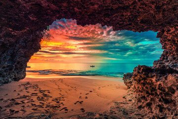 Beautiful view from mountain cave to tropical beach with colorful sunset above the ocean