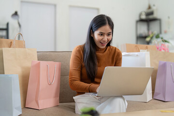 Exciting online shopping moment. Woman using laptop and credit card while sitting among shopping bags in her living room.
