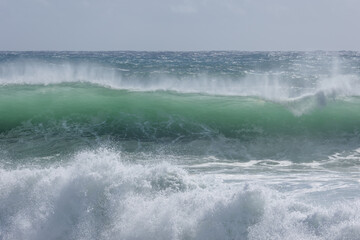 A green faced wave that is cresting and about to break looms over boiling surf driven by an approaching cyclone or hurricane at Snapper rocks at Coolangatta on the Gold Coast in Queensland, Australia.