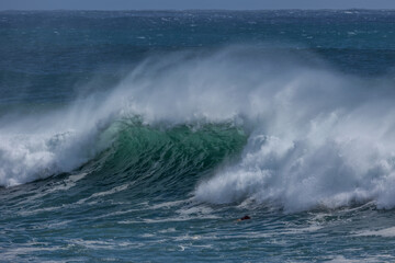 A massive green faced wave breaking on either side with wind spray and a diving surfer with the wave being driven by the edge of a cyclone or hurricane at Coolangatta on the Gold Coast in Australia.