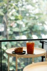 Cup of iced black coffee with a piece of banana bread cake on table by the window.