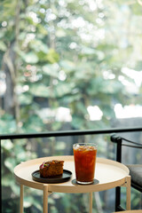 Cup of iced black coffee with a piece of banana bread cake on table by the window.