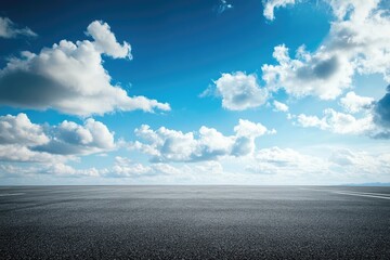 Empty asphalt road stretches under a vibrant blue sky dotted with fluffy white clouds