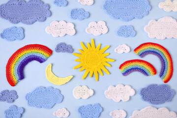Fototapeta premium Knitted toys blue and white clouds, yellow sun, rainbow, moon on blue background. Baby stuff and accessories. Top view, flat lay, banner