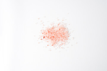 Pink colored Himalayan coarse salt (halite) scattered on the table. Isolated on white background.