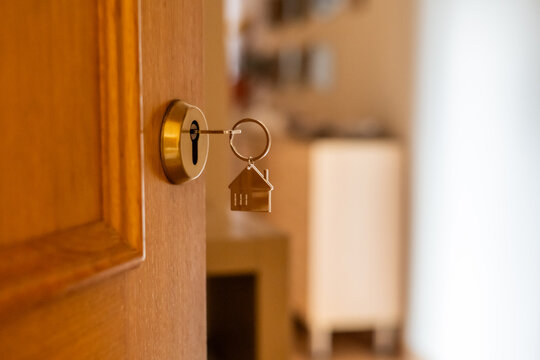 Golden key with a small house keychain opening a wooden door, symbolizing the purchase or rental of a new property, representing real estate investment and homeownership