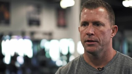 Middle-Aged Caucasian Male Fitness Trainer Discussing Workout Techniques in a Modern Gym Setting