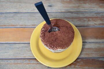 Italian dessert Tiramisu in glass cup and spoon on saucer in sunlit cafe.