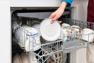 Close-up of female takes of clean dish out of dishwasher machine	