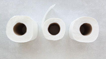 Three rolls of white toilet paper are in a row on the table, top view. Disposable paper towels for hands. Sanitary napkins.