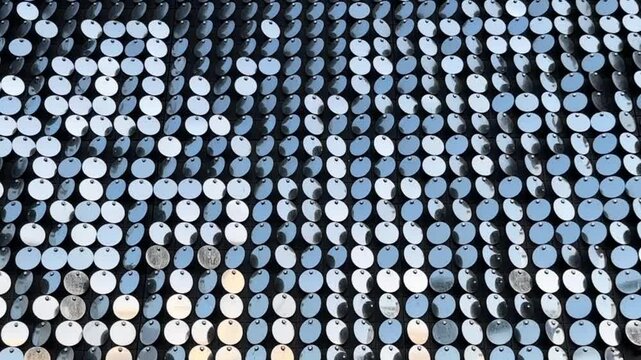 Metallic, reflective, circular discs, sequins or reflective panels, arranged in a grid pattern. Each disc reflects light in a dynamic way