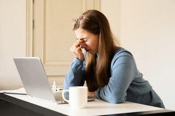 Tired overload young woman suffering from eye strain feeling headache working on a computer at home office. Unhealthy student girl having dry eyes syndrome. The impact of screens on vision digital era